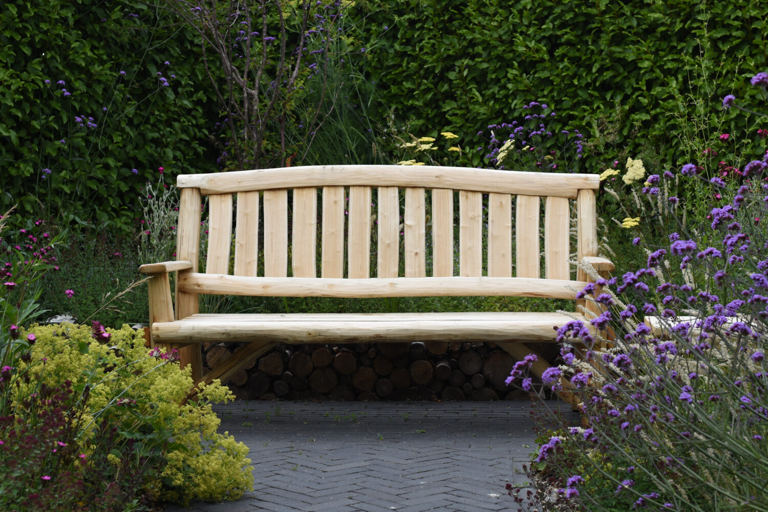Handcrafted Chestnut Wood Bench at the end of a clay paver path nestled among naturalistic planting